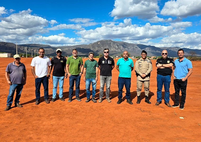 Grupo de nove representantes, incluindo membros da SSP-BA, Prefeitura e Polícias Civil e Militar, inspecionando o terreno de terra vermelha para a Unidade Integrada das Polícias em Livramento de Nossa Senhora.