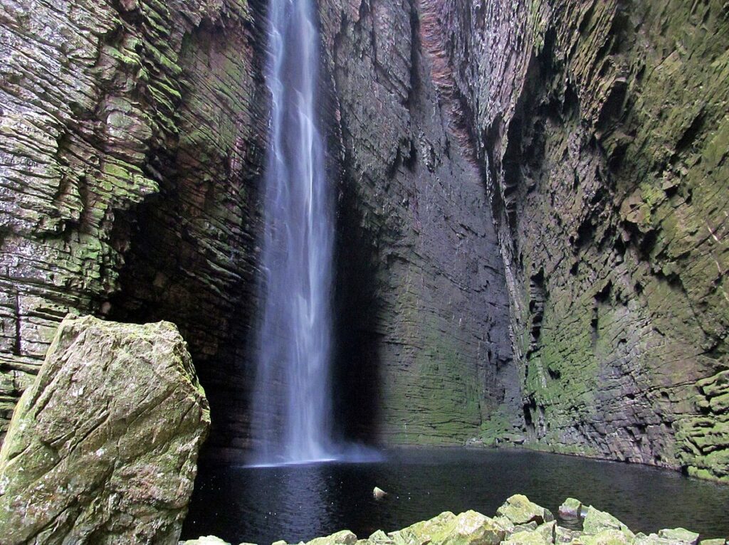 Cachoeira da Fumacinha: uma impressionante queda d'água cercada por paredões rochosos e vegetação densa, localizada em um cenário remoto.