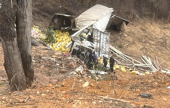 Caminhão virado de lado após acidente em área montanhosa da BA-148; vegetação ao redor e presença de socorristas em operação de resgate.