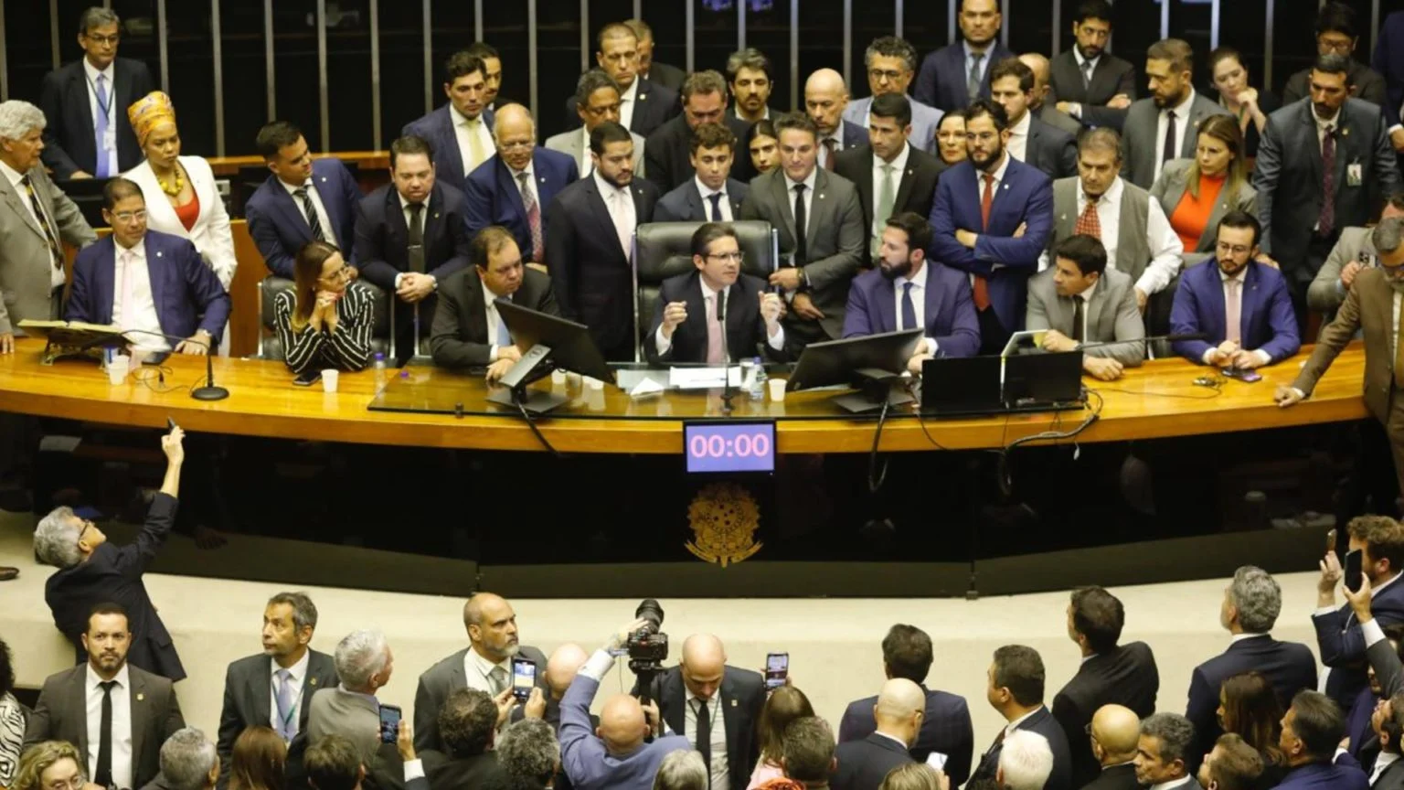 Hugo Motta conduz os trabalhos no plenário nesta quarta-feira (6.ago.2025), enquanto deputados da oposição permanecem posicionados atrás da Mesa Diretora após dois dias de ocupação.