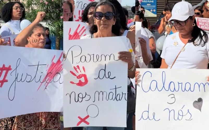 Mulheres vestidas de branco seguram cartazes com frases como “Calaram três de nós” e “Parem de nos matar” durante protesto em Ilhéus, Bahia, após o assassinato de três mulheres na Praia dos Milionários.